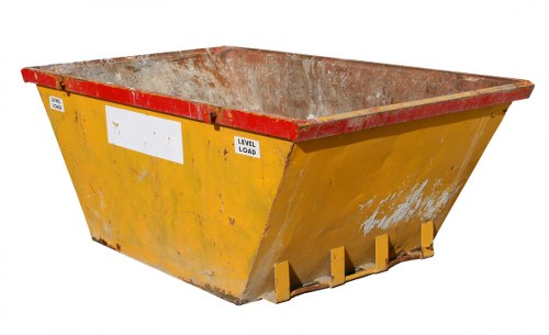 A large, industrial metal skip with a rectangular shape and reinforced red top edge, positioned outdoors on a paved area likely used for waste disposal or rubbish removal. The skip's body is painted bright yellow, though the surface shows signs of dirt, rust, and chipped paint revealing the underlying metal, indicating extensive use. The interior of the skip is visible and appears stained and worn from previous loads, with a rough, textured finish. Situated on a flat surface, the skip is supported by yellow metal feet at the base for stability. In the background, there are no distinct environmental features visible, focusing solely on the skip itself. The image conveys a professional context of waste management, suitable for a rubbish removal service such as Commercial Waste Lambeth, serving properties in and around Lambeth, London, with the skip potentially positioned on a commercial or residential premises undergoing rubbish clearance.